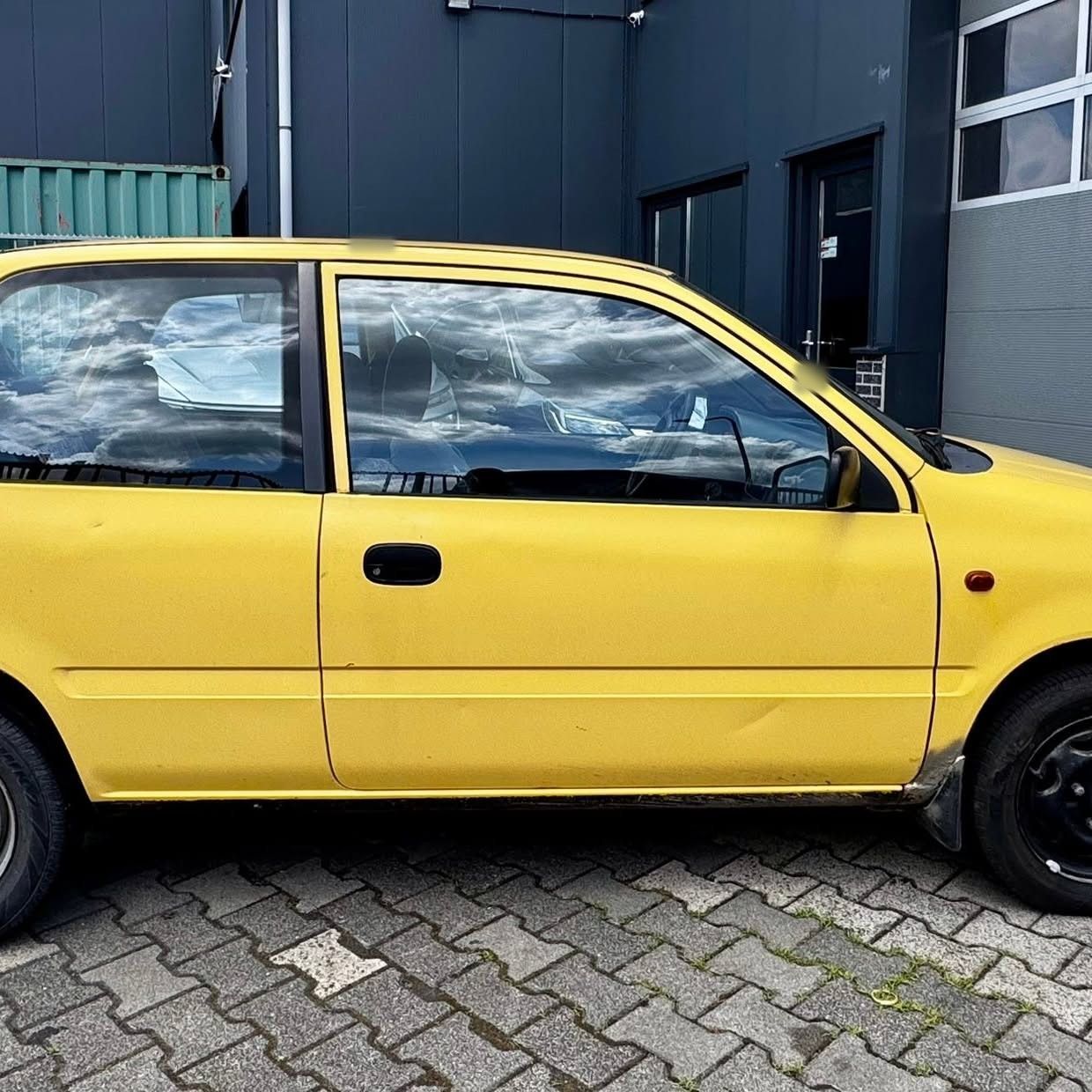 Zijkant van een gele Suzuki tegen het pand van Fix2Drive
